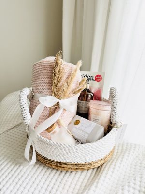 Luxury pink spa gift basket titled The Blush and Bloom by Divine Bloom Sarasota, featuring a pink chenille throw blanket, Castelbel goat milk soap, amber liquid soap, and a pink jasmine santal candle in a woven rope basket.